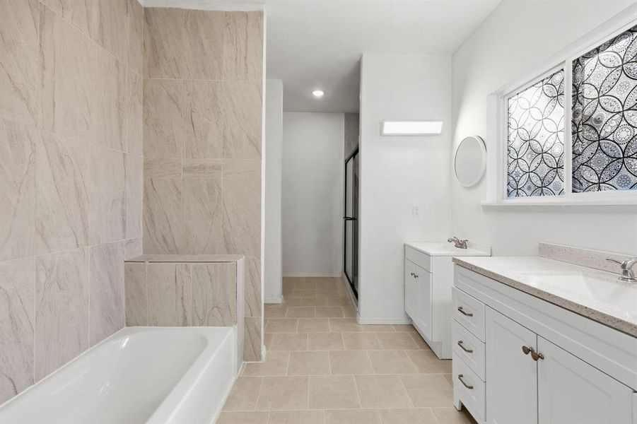 Primary ensuite bathroom with dual vanities, separate tub and shower and light tile patterned floors