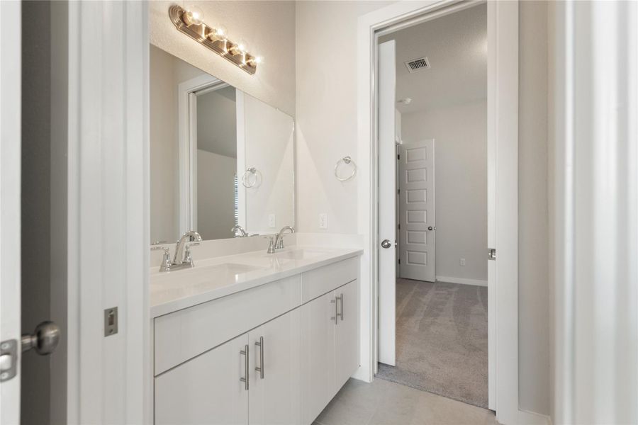 Bathroom with double vanity, light colored carpet, and light tile patterned floors