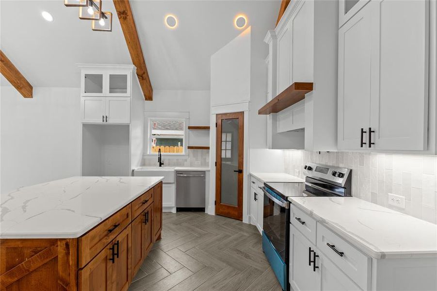 Kitchen featuring tasteful backsplash, appliances with stainless steel finishes, lofted ceiling with beams, white cabinetry, and light stone counters