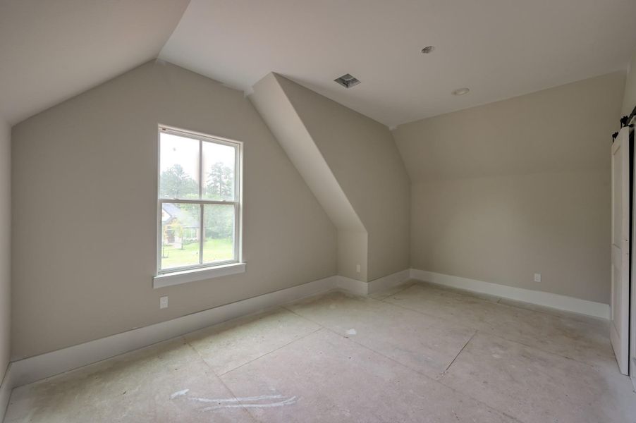 This room features neutral walls, a large window with a view of greenery, and sloped ceilings, creating a cozy atmosphere.  Perfect for a bedroom, gym or guests.