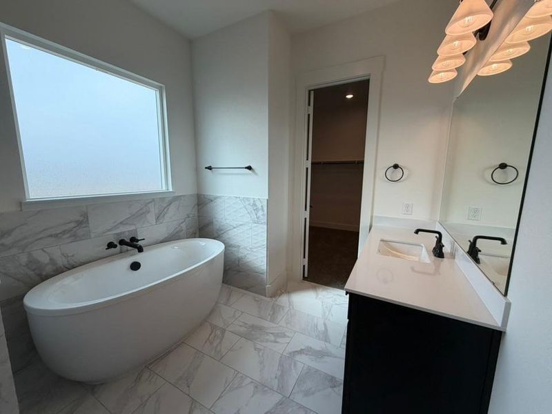 Bathroom with a freestanding bath, tile walls, a walk in closet, light marble finish flooring, and vanity