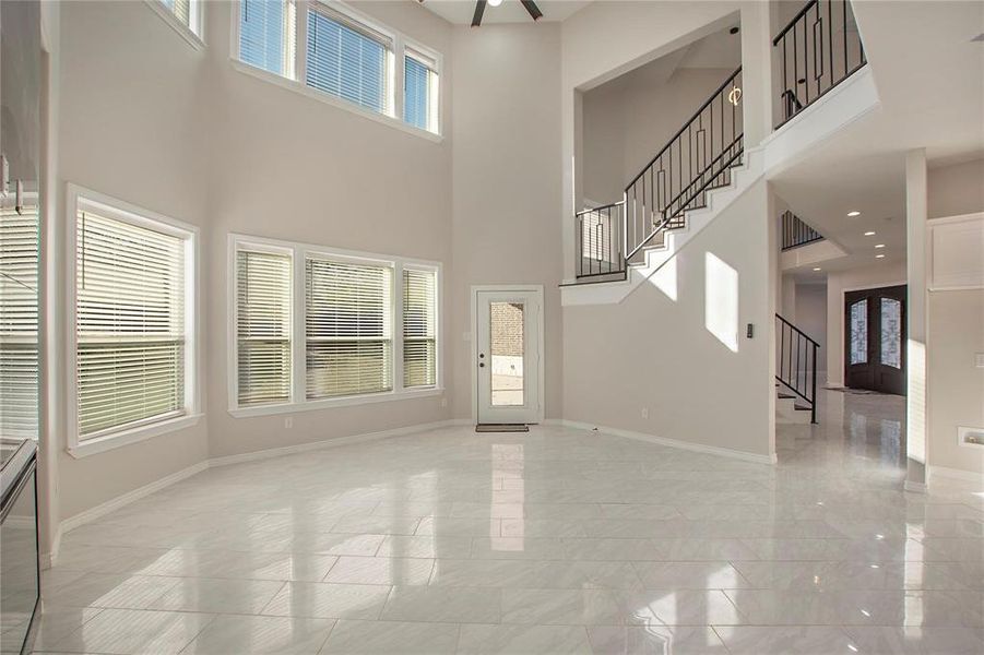 Unfurnished living room featuring a high ceiling, stairs, and light marble finish flooring Unfurnished living room featuring a high ceiling, stairs, and light marble finish flooring