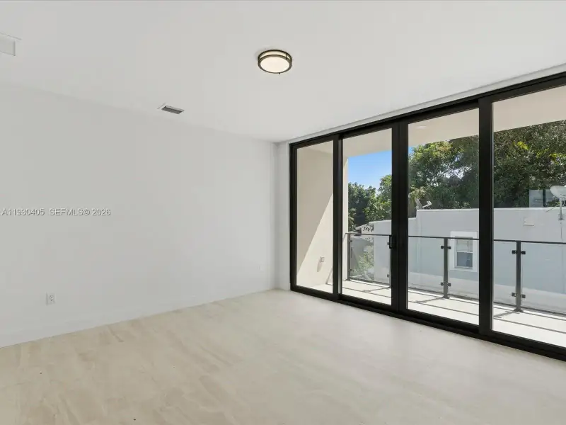 Floor-to-ceiling multi-panel sliding glass doors, neutral stone-finish flooring, recessed ceiling lighting, and a private balcony with glass and metal railings Floor-to-ceiling multi-panel sliding glass doors, neutral stone-finish flooring, recessed ceiling lighting, and a private balcony with glass and metal railings
