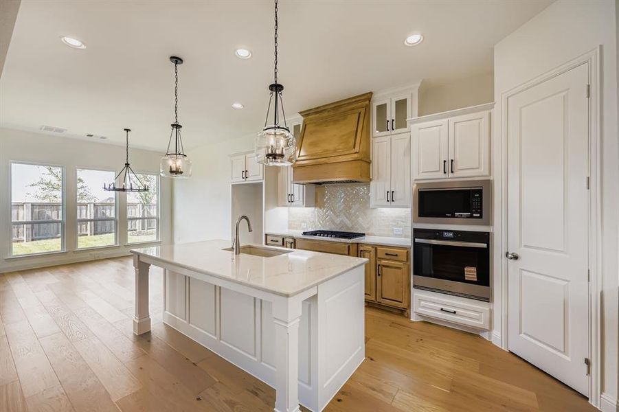 Kitchen with white cabinets, tasteful backsplash, oven, a center island with sink, and pendant lighting