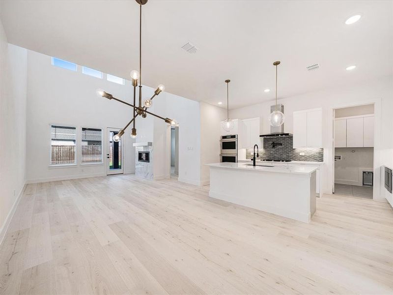 Kitchen with white cabinetry, decorative backsplash, a center island with sink, light wood finished floors, and open floor plan