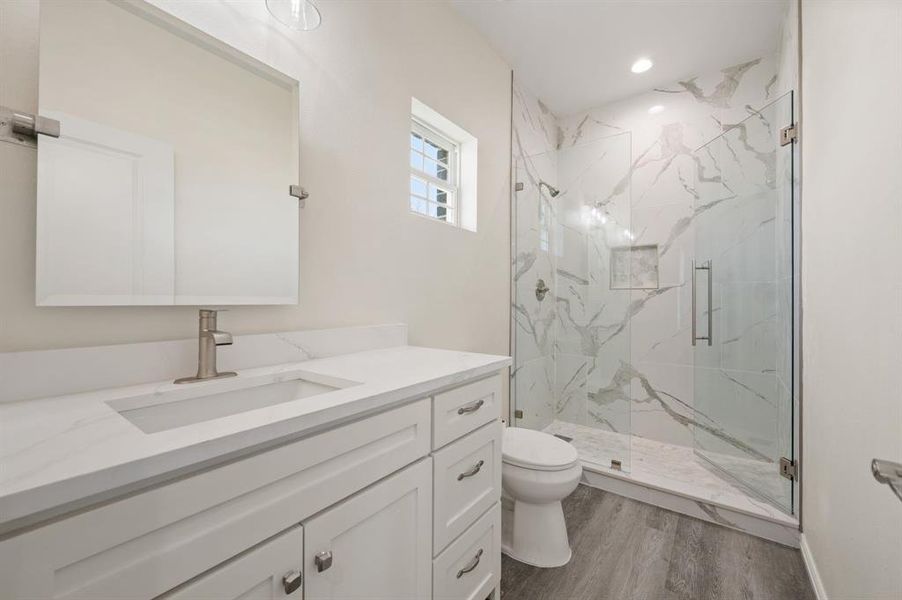 Bathroom with a marble finish shower, vanity, and dark wood-style floors Bathroom with a marble finish shower, vanity, and dark wood-style floors