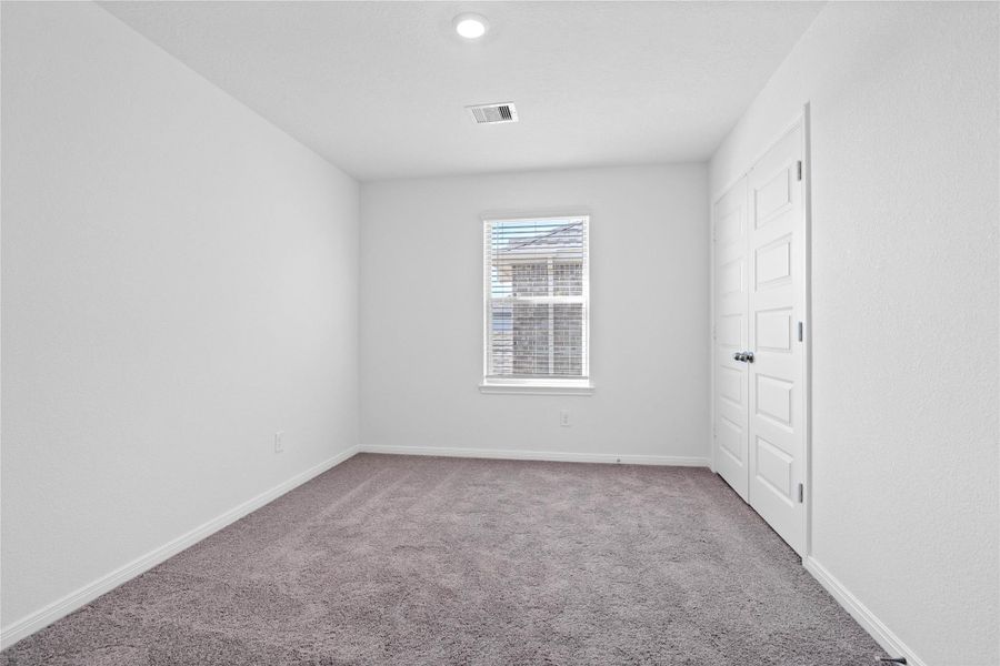 This secondary bedroom offers comfort and style with plush carpeting, neutral paint tones, recessed lighting, large window with blinds, and a generously sized closet.