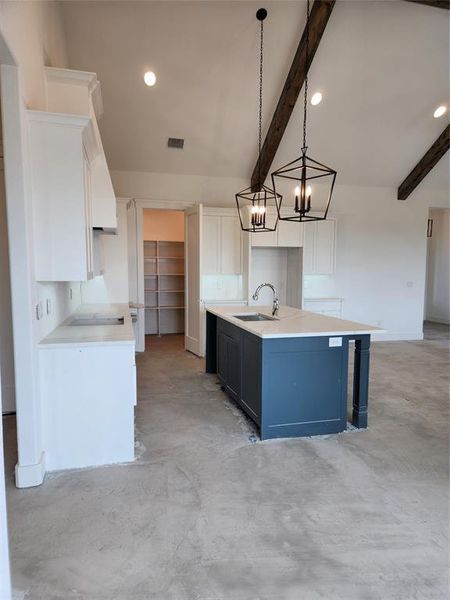 Kitchen with a center island with sink, white cabinets, sink, and decorative light fixtures