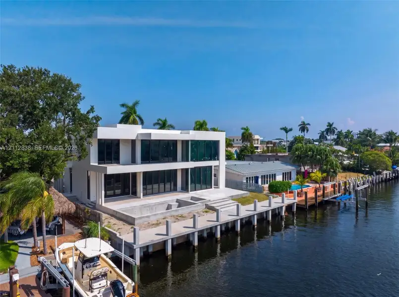Modern two-story waterfront residence featuring an expansive rear patio, concrete dock, floor-to-ceiling glass paneling, and flat roof architecture Modern two-story waterfront residence featuring an expansive rear patio, concrete dock, floor-to-ceiling glass paneling, and flat roof architecture