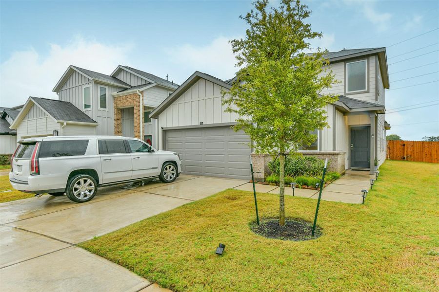 Modern one year old two-story house with a gray facade, attached garage, and a well-maintained front yard. It features a paved driveway and a small tree in the front. Ideal for family living in a suburban neighborhood.