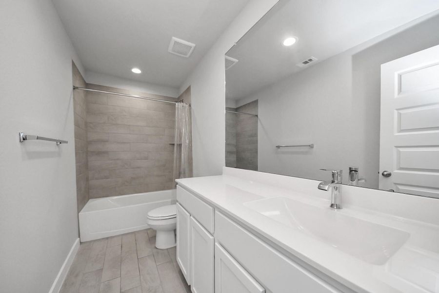 Full bathroom with a spacious vanity and a tub/shower combo with tile surround, conveniently located off the hallway across from the kitchen and shared by bedrooms two and three.