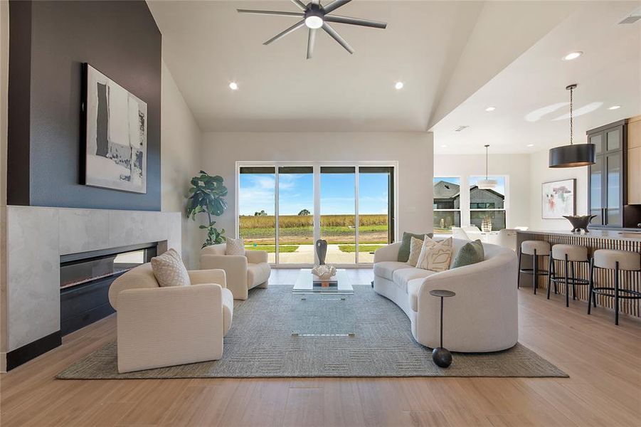 Living room with a glass covered fireplace, light wood finished floors, recessed lighting, a ceiling fan, and vaulted ceiling Living room with a glass covered fireplace, light wood finished floors, recessed lighting, a ceiling fan, and vaulted ceiling