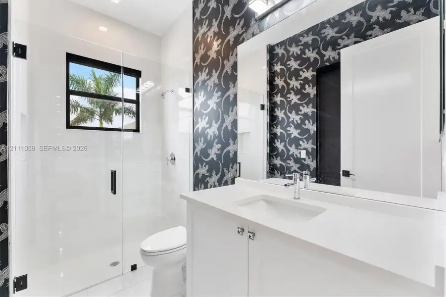 Bathroom featuring a white vanity with a quartz countertop, frameless glass-enclosed shower, polished chrome fixtures, and patterned wallcovering