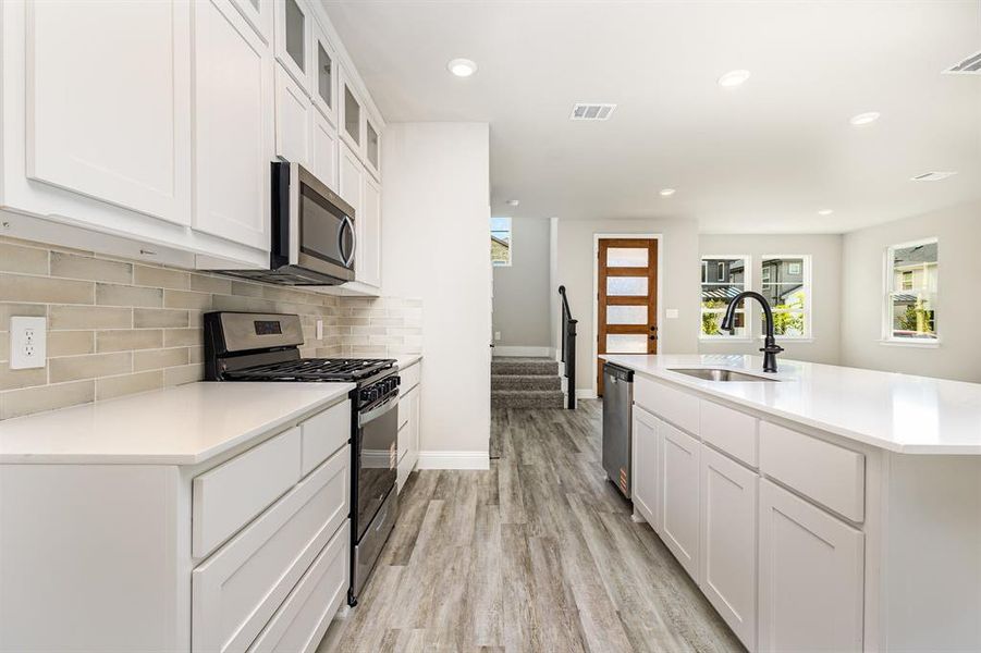 Kitchen featuring stainless steel appliances, glass insert cabinets, white cabinetry, recessed lighting, and tasteful backsplash
