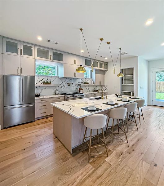 Kitchen featuring decorative backsplash, a breakfast bar, appliances with stainless steel finishes, a large island with sink, and light wood-style flooring Kitchen featuring decorative backsplash, a breakfast bar, appliances with stainless steel finishes, a large island with sink, and light wood-style flooring