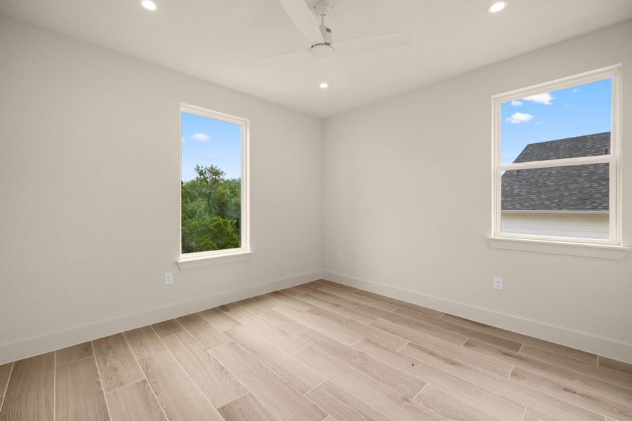 Recessed lighting and a ceiling fan create a bright, comfortable atmosphere in this ample bedroom.