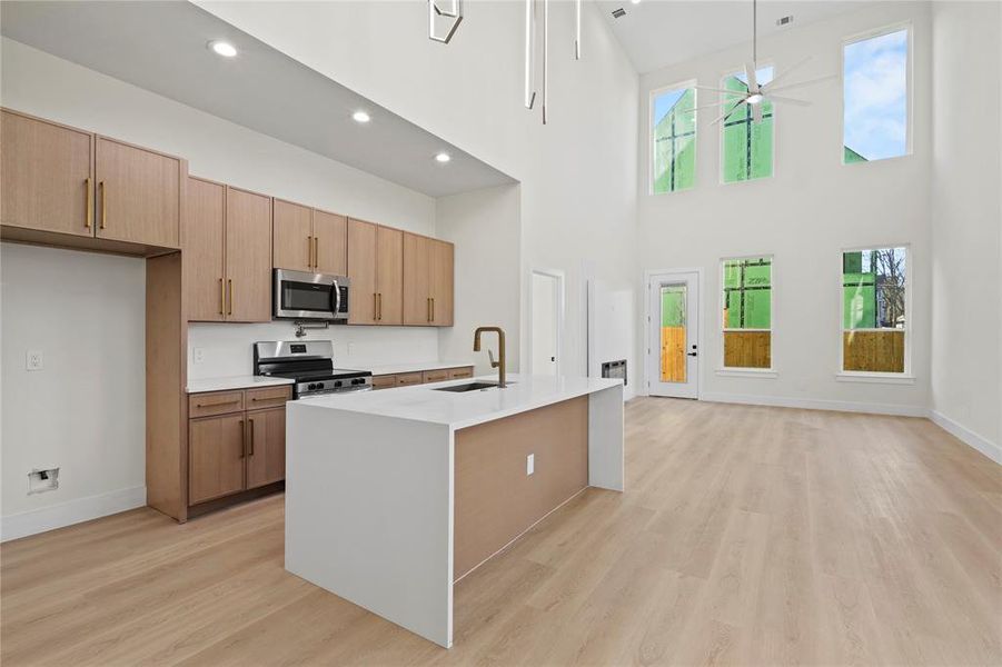 Kitchen with ceiling fan, a kitchen island with sink, light countertops, appliances with stainless steel finishes, and light wood finished floors