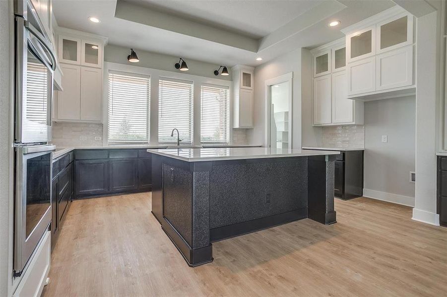 Kitchen featuring a tray ceiling, white cabinets, a center island, light hardwood / wood-style floors, and backsplash