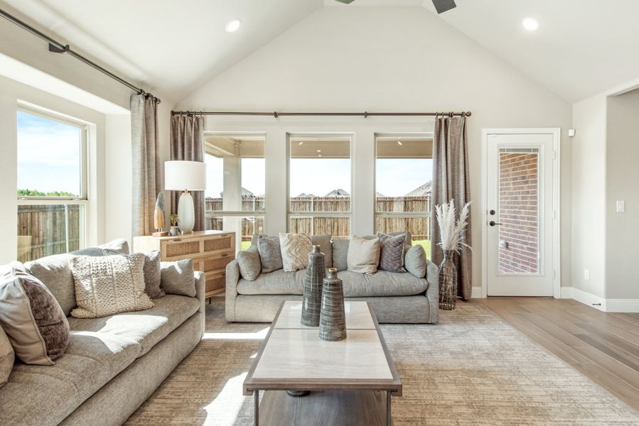 Living room with vaulted ceiling, two gray sofas, hardwood floors, and large windows with backyard views