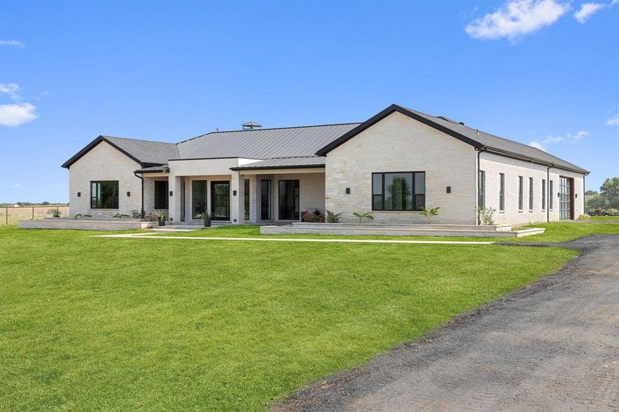 Rear view of property featuring a lawn, covered
porch, a metal roof, stone siding, and brick siding Rear view of property featuring a lawn, covered
porch, a metal roof, stone siding, and brick siding