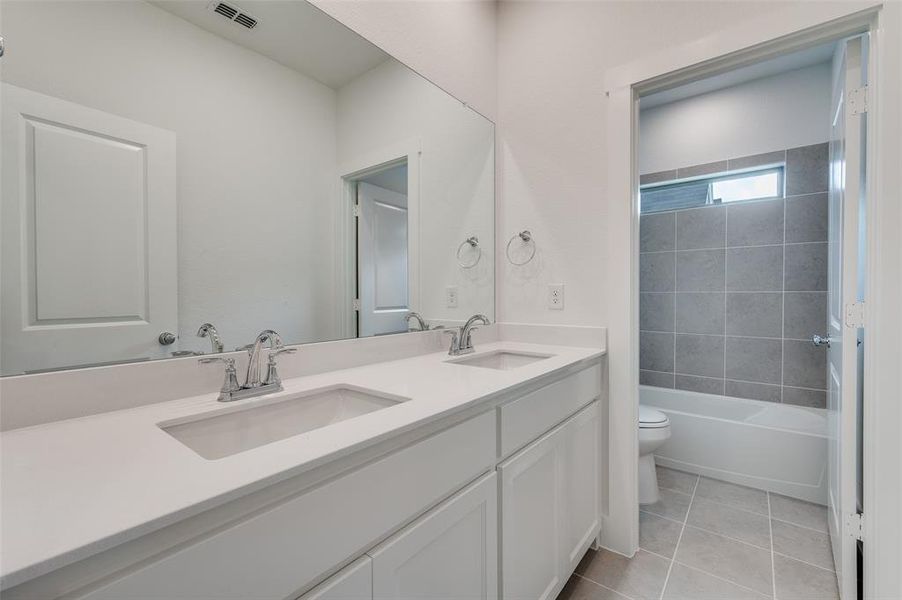 Full bathroom with toilet, tiled shower / bath combo, vanity, and tile patterned floors