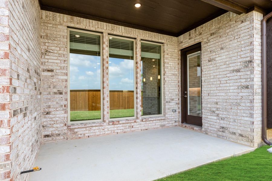 Covered back patio with light brick walls, large windows, and a glass back door leading inside. Covered back patio with light brick walls, large windows, and a glass back door leading inside.