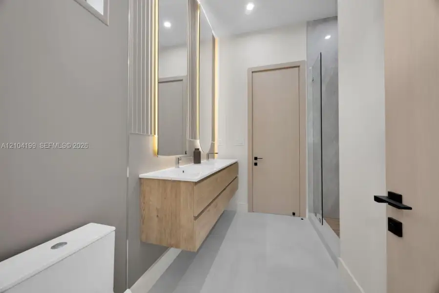 Floating wood-finish double vanity with integrated sinks, dual backlit mirrors, matte black hardware, and a walk-in shower with large-format tile surround