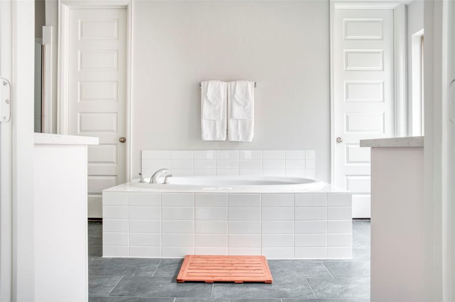This bathroom features a sleek, modern design with a large white tiled bathtub at the center, flanked by two closed doors, gray tile flooring, and a minimalist palette. This bathroom features a sleek, modern design with a large white tiled bathtub at the center, flanked by two closed doors, gray tile flooring, and a minimalist palette.