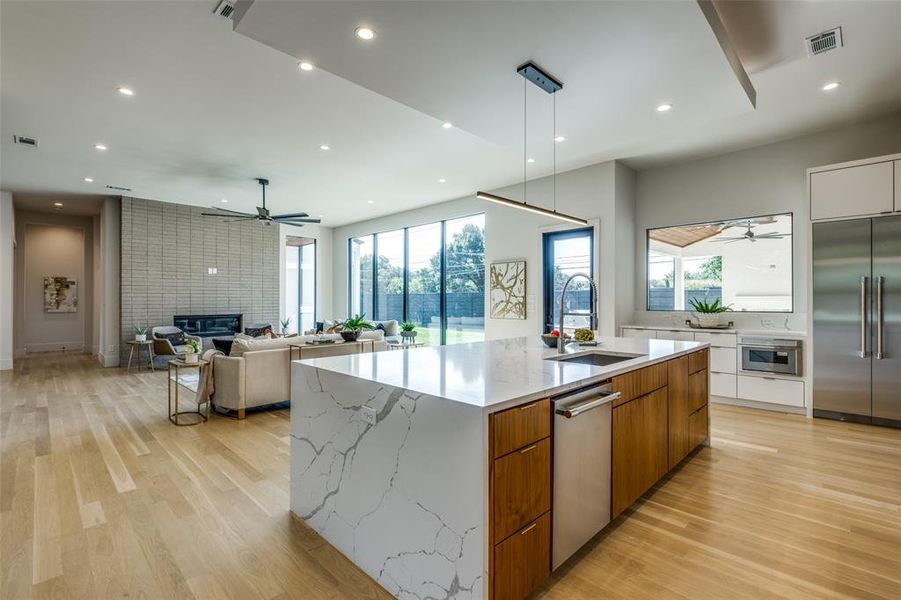 Kitchen featuring a fireplace, appliances with stainless steel finishes, an island with sink, sink, and ceiling fan