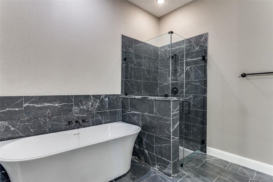 Bathroom featuring a marble finish shower, a soaking tub, tile walls, and dark marble finish floors Bathroom featuring a marble finish shower, a soaking tub, tile walls, and dark marble finish floors