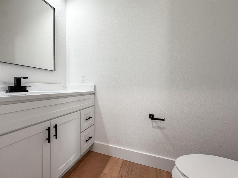 Half bath with vanity, wood finished floors, toilet, and baseboards