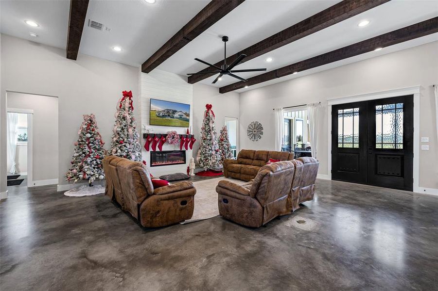 Living room featuring finished concrete flooring, ceiling fan, a large fireplace, french doors, and recessed lighting Living room featuring finished concrete flooring, ceiling fan, a large fireplace, french doors, and recessed lighting