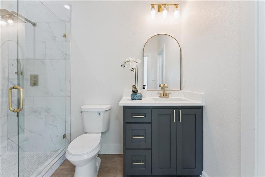 Full bath with vanity, a marble finish shower, and wood finished floors