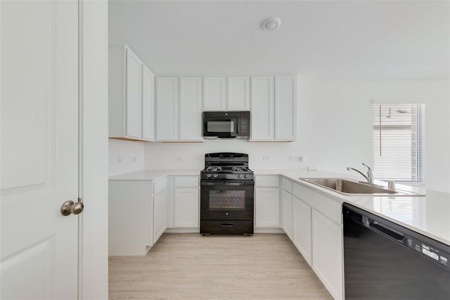 Kitchen featuring light wood-type flooring, white cabinetry, sink, and black appliances