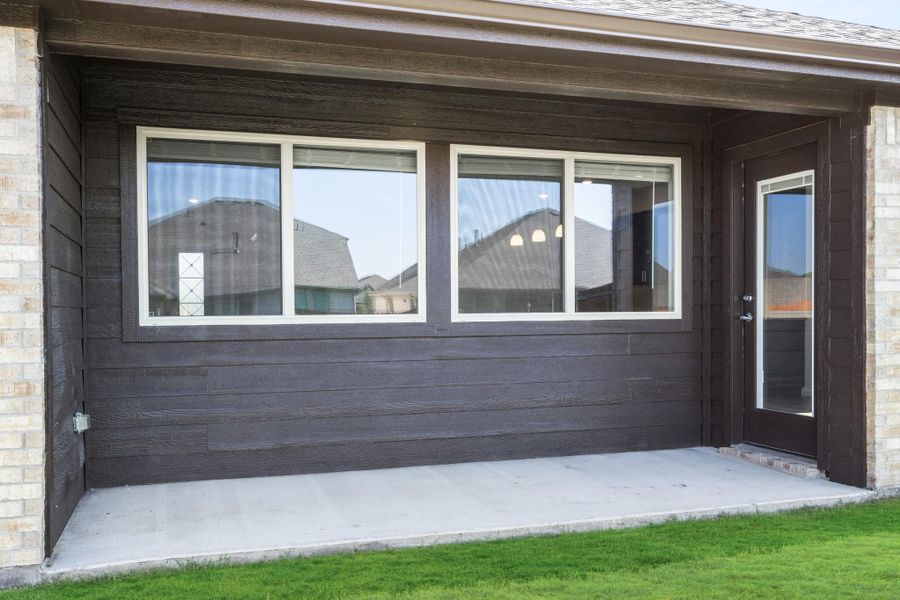 Covered back patio with dark wood siding, large windows, and a side entry door on concrete slab