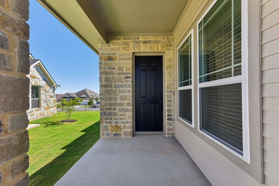 View of exterior entry featuring stone siding, a yard, and a patio area