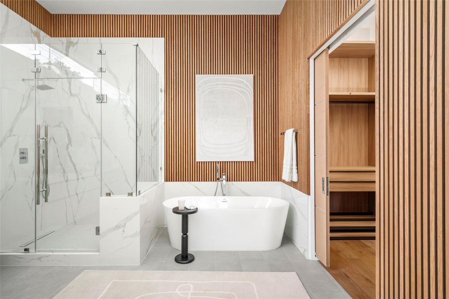 [First Floor Ensuite Bath] Downstairs bathroom with oversized 71" soaking tub, frameless Calacatta Oro shower, and spacious walk-in closet.