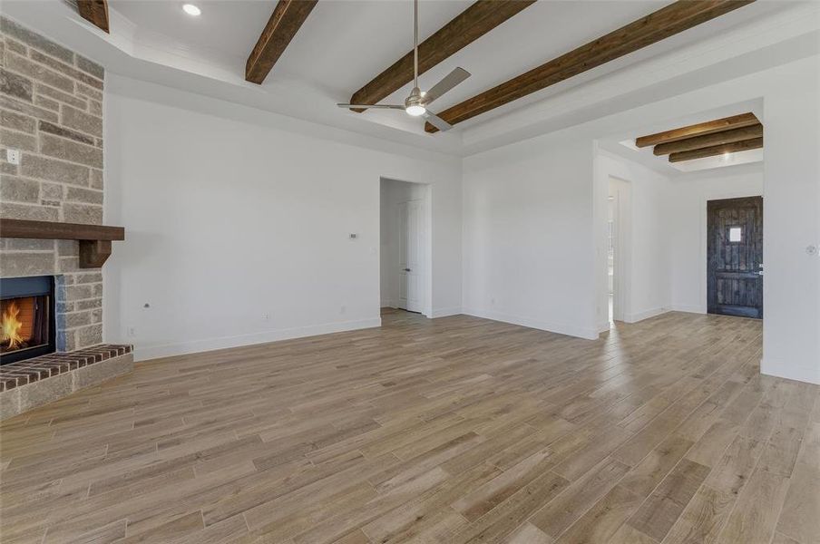 Spacious room featuring wood-finish flooring, a stone fireplace with a wood mantle, and exposed wood ceiling beams