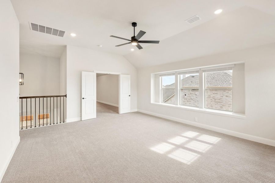 Spacious bonus room with vaulted ceiling, ceiling fan, carpet flooring, and large windows near staircase railing