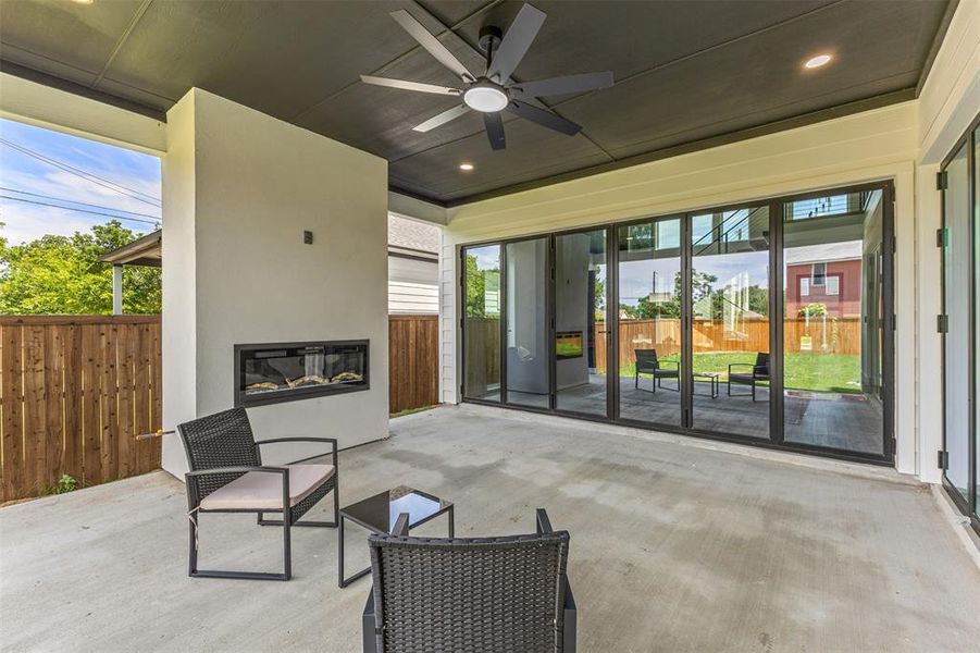 Covered outdoor patio with a built-in linear fireplace, concrete flooring, and a ceiling fan