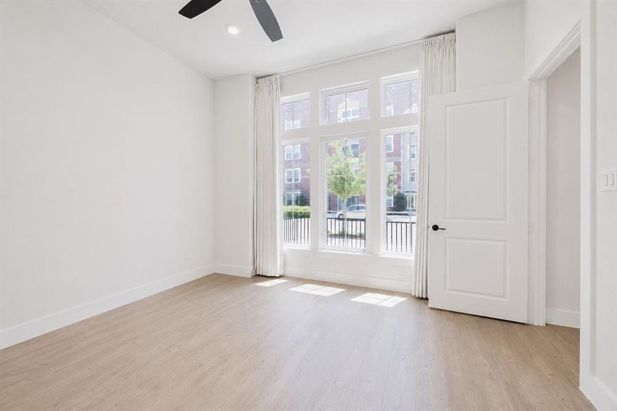 Bright room featuring large multi-pane windows, wood-finish flooring, a ceiling fan, and white trim