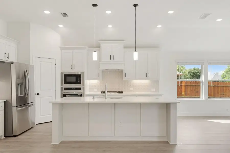 White kitchen with large center island, pendant lights, stainless steel appliances, and light wood floors