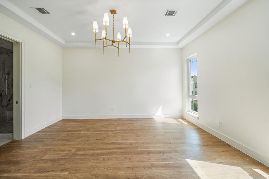 Natural light filled and spacious primary bedroom with wood flooring, a modern chandelier, and ample natural light from a large window.