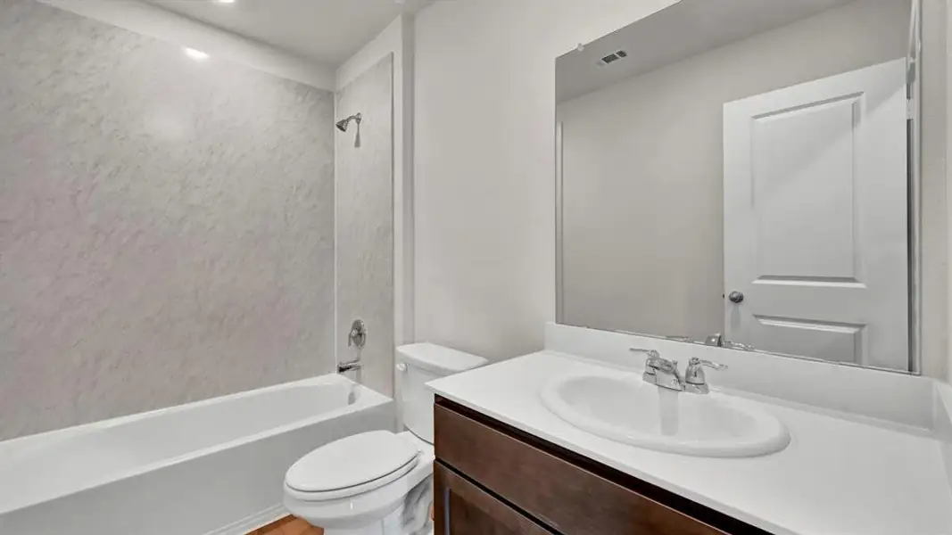 Contemporary bathroom featuring a white tub with shower, marble-finish wall surround, single-sink vanity with white countertop, dark wood-finish cabinetry, and chrome fixtures