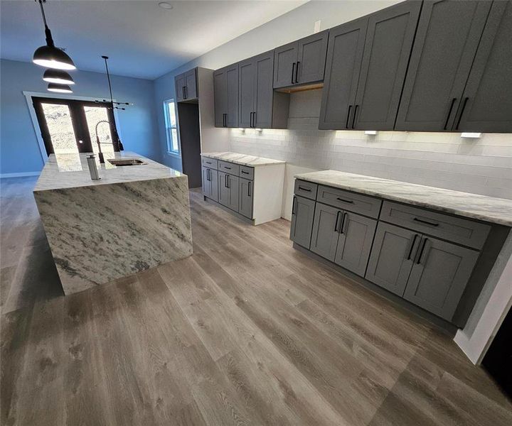 Kitchen with gray cabinets, light stone counters, light wood-type flooring, and backsplash Kitchen with gray cabinets, light stone counters, light wood-type flooring, and backsplash