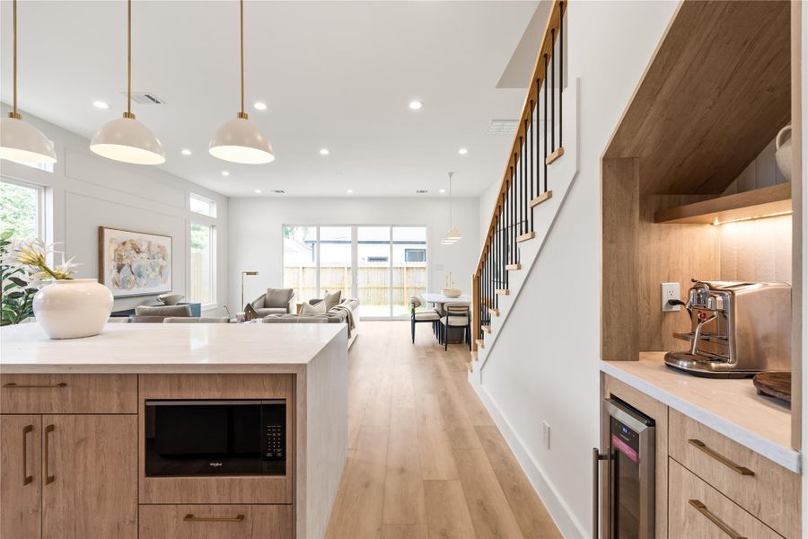 A built-in coffee bar nook sits just off the kitchen with under-cabinet lighting and a wine fridge, giving you a dedicated spot for that daily ritual without crowding the main kitchen. The open sightline to the stairs and living area keeps everything connected.