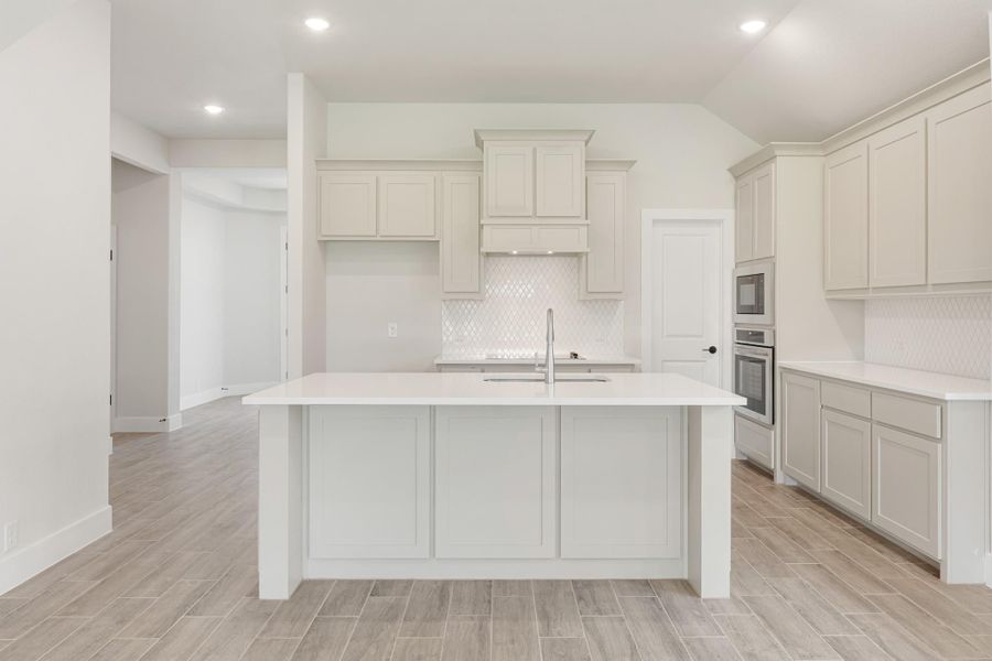 White kitchen with large center island, light gray cabinets, tile backsplash, and wood-look floors