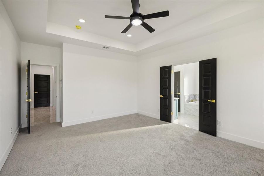 Empty room featuring ceiling fan, a raised ceiling, and light colored carpet