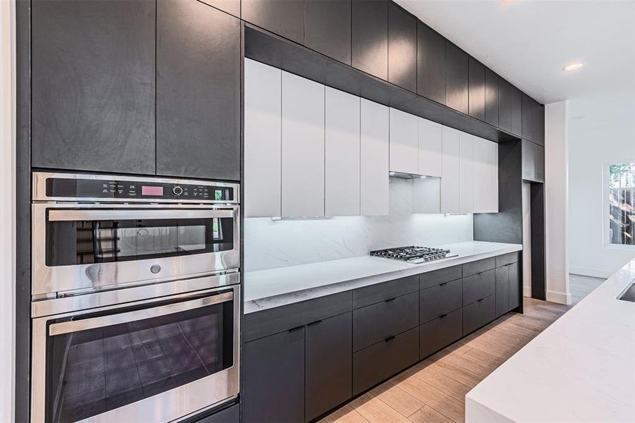 Kitchen featuring white cabinets, modern cabinets, appliances with stainless steel finishes, light wood finished floors, and light stone counters