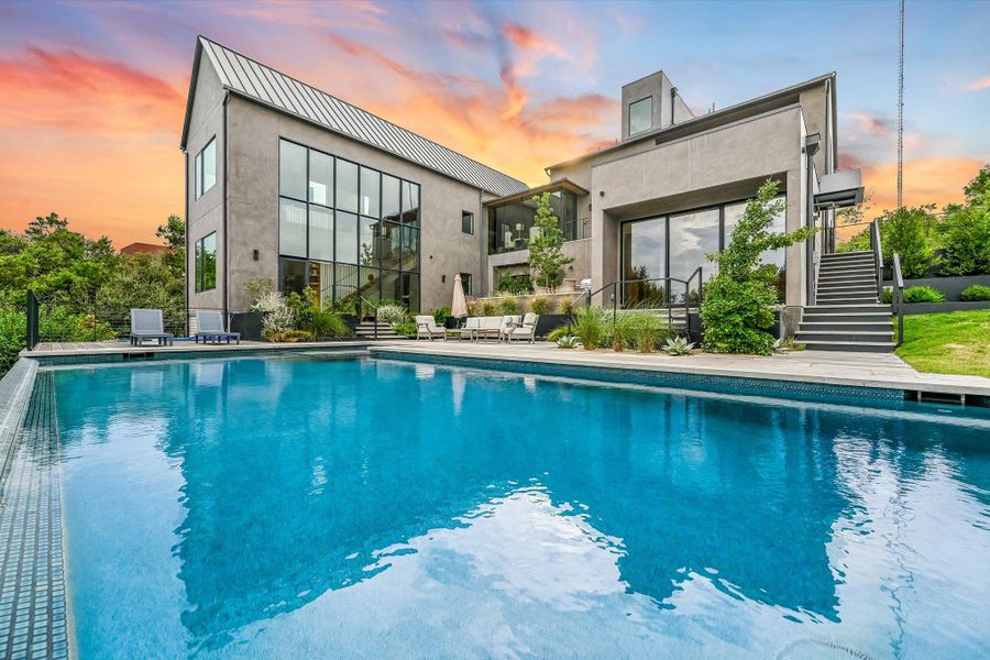 Back of property at dusk featuring stairway, an outdoor pool, a patio area, and a metal roof